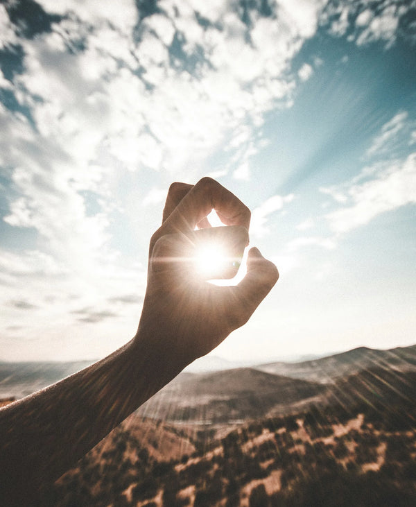 Human hand on sky background creating circle around the sun in focus